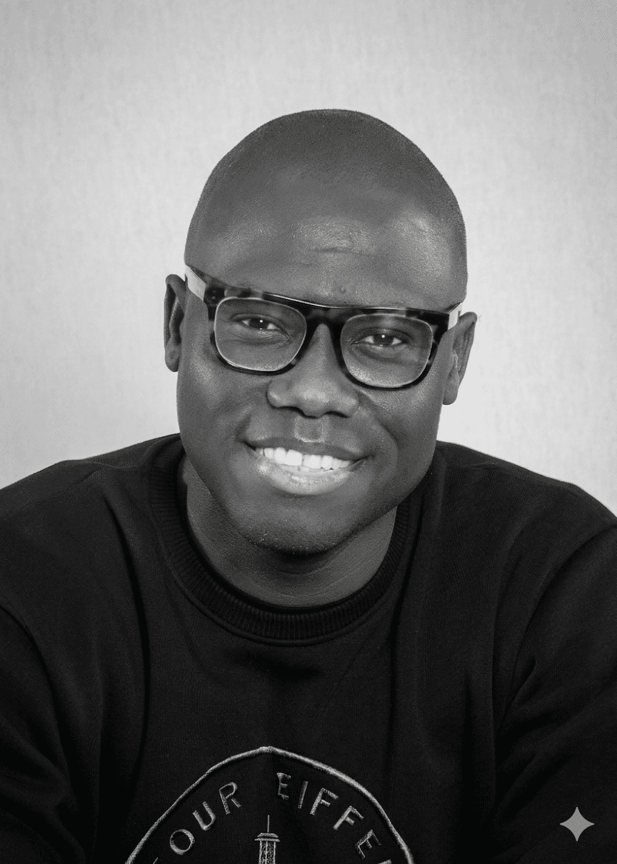 Smiling bald Black man wearing thick-rimmed glasses in a black and white close-up portrait.